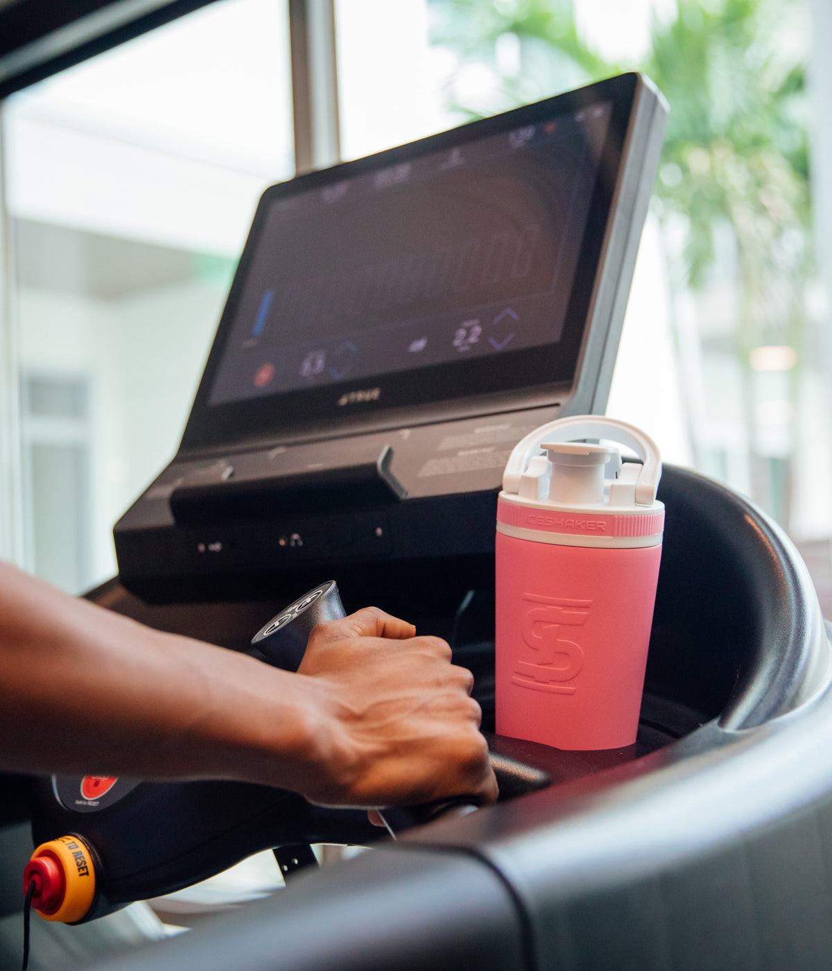 This image shows a Pink 26oz Ice Shaker being stored in a treadmill cup holder to show that the 26oz Ice Shaker fits in all standard size cup holders.