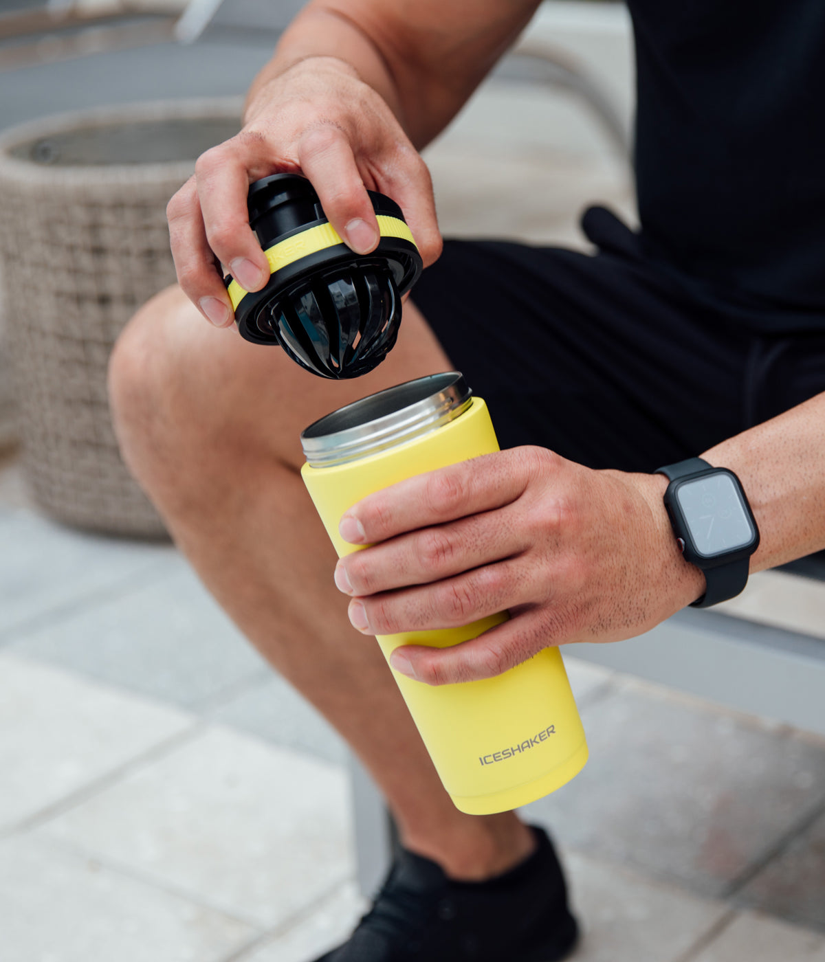 This image shoes the Yellow 26oz Ice Shaker being opened by an man. The close up view of the 26oz Ice Shaker shows the lid being twisted off, revealing the patented lid and agitator combo. The other hand holds the 26oz Yellow Insulated Bottle.