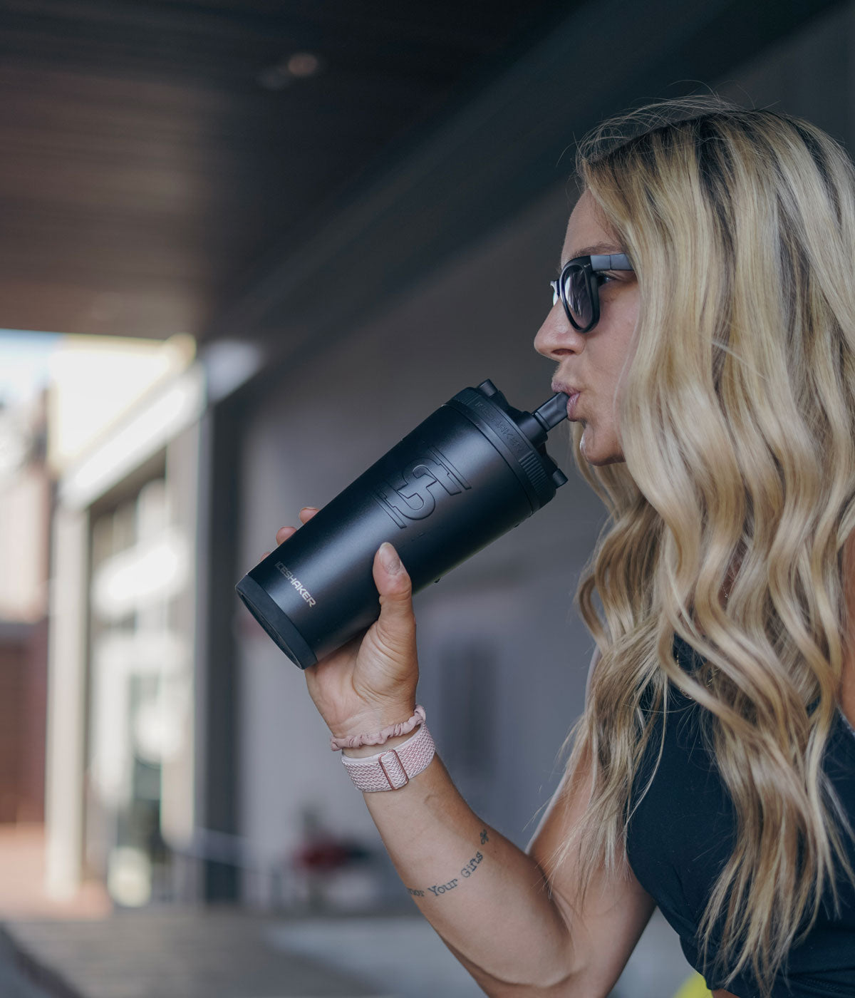 An image of a woman with sunglasses on taking a drink from the Flip Up Sport Straw on a black-colored 26oz Sport Bottle