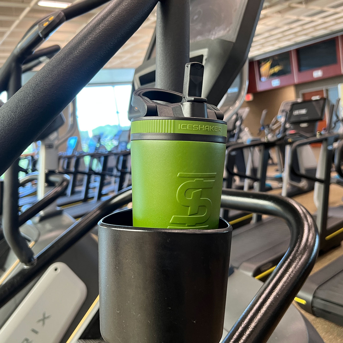 an image of a Green-colored 26oz Sport Bottle fitting into a cup holder on a treadmill. 