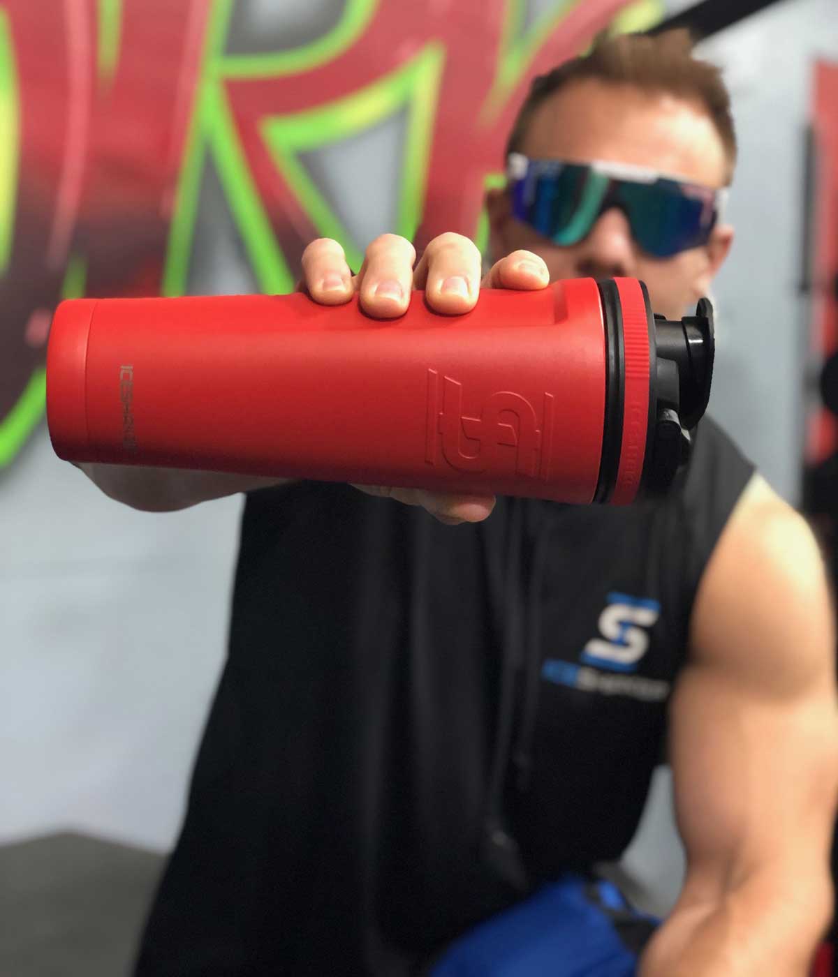 Ice Shaker CEO, Chris Gronkowski holds out the red-colored 36oz Ice Shaker sideways, right in front of the camera. The 36oz Ice Shaker is partially blocking his face.