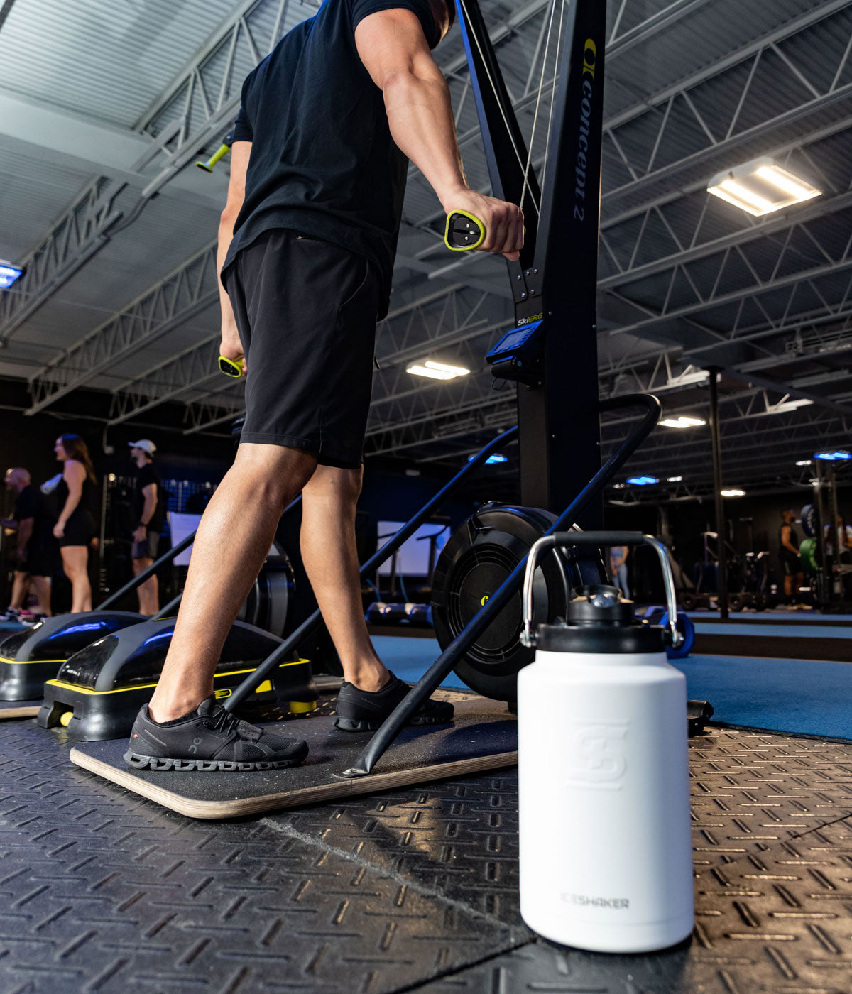 An image of a White-colored Half Gallon Jug sitting on the floor of a gym. In the background, a man is using a machine to workout.