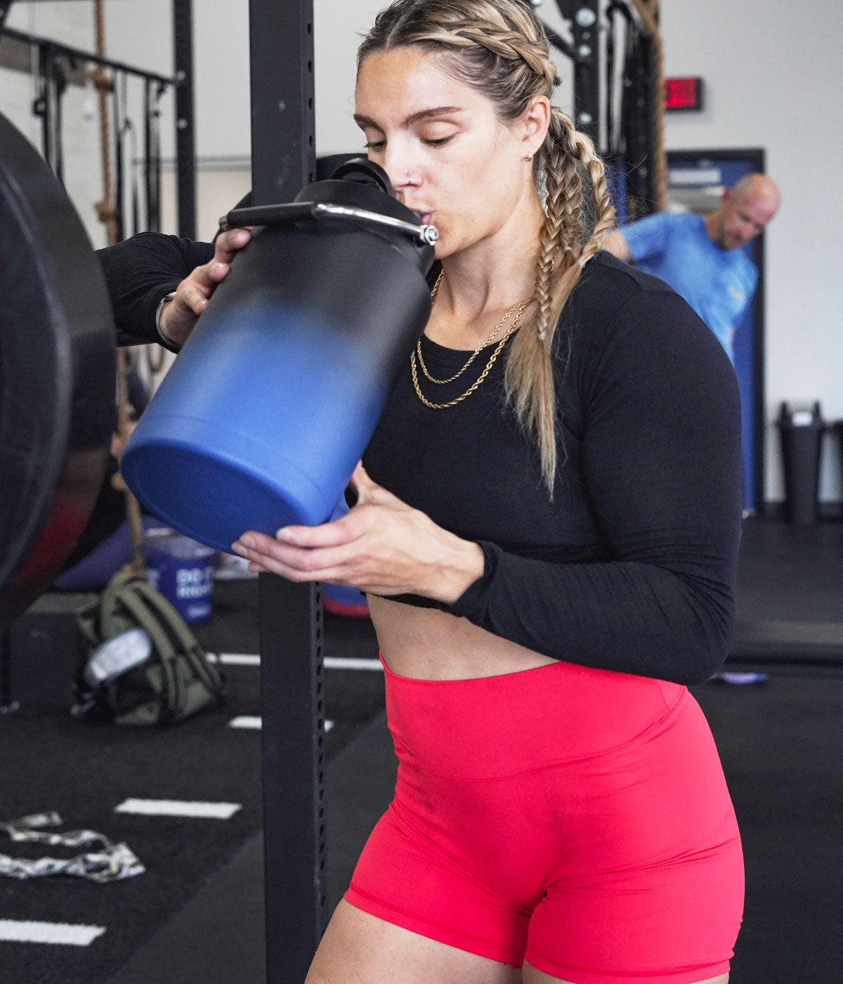 A woman who has been working out takes a drink from a Navy Black Ombre-colored One Gallon Jug.