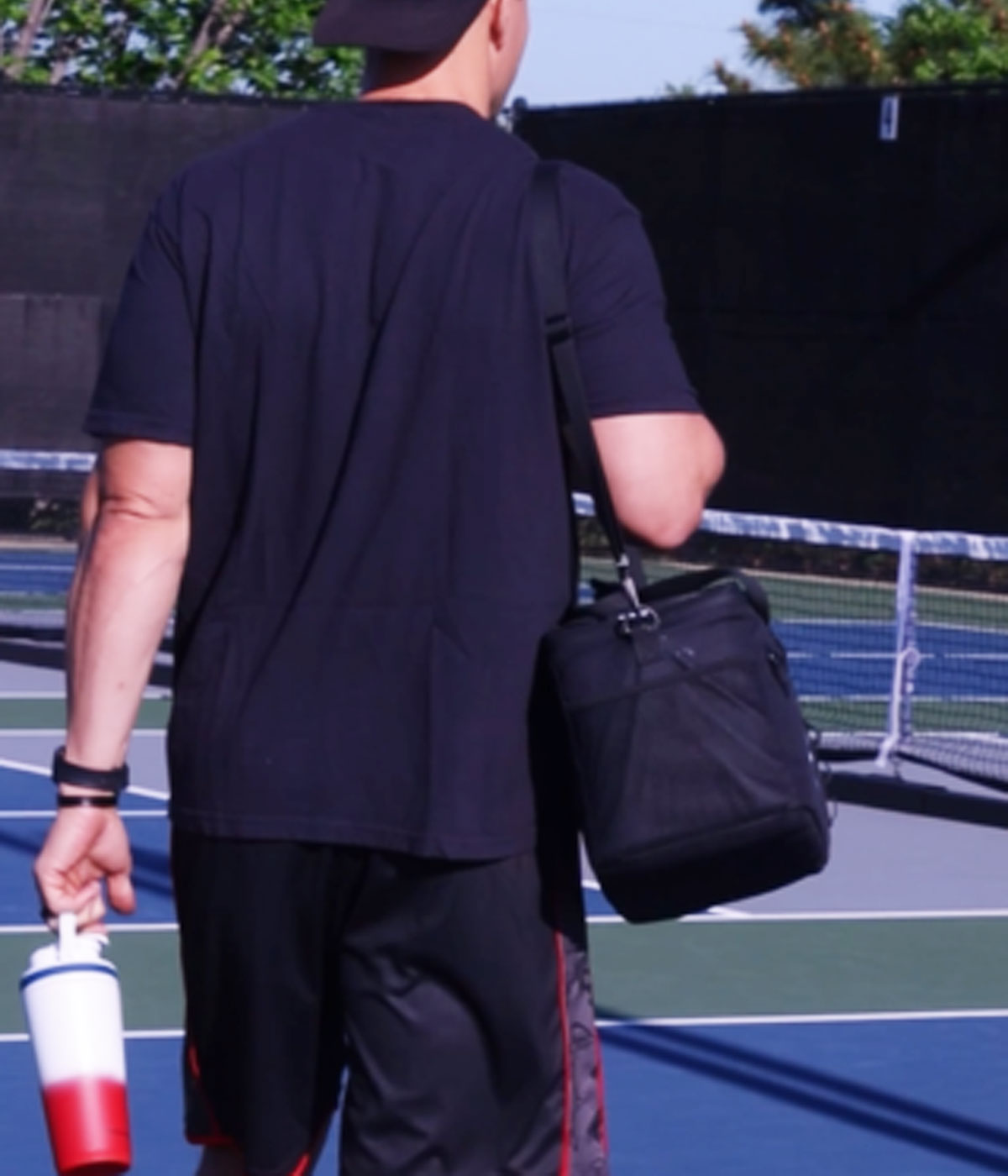 This image shows a man carrying The Duffel by its shoulder strap as he walks onto a Pickle Ball court.