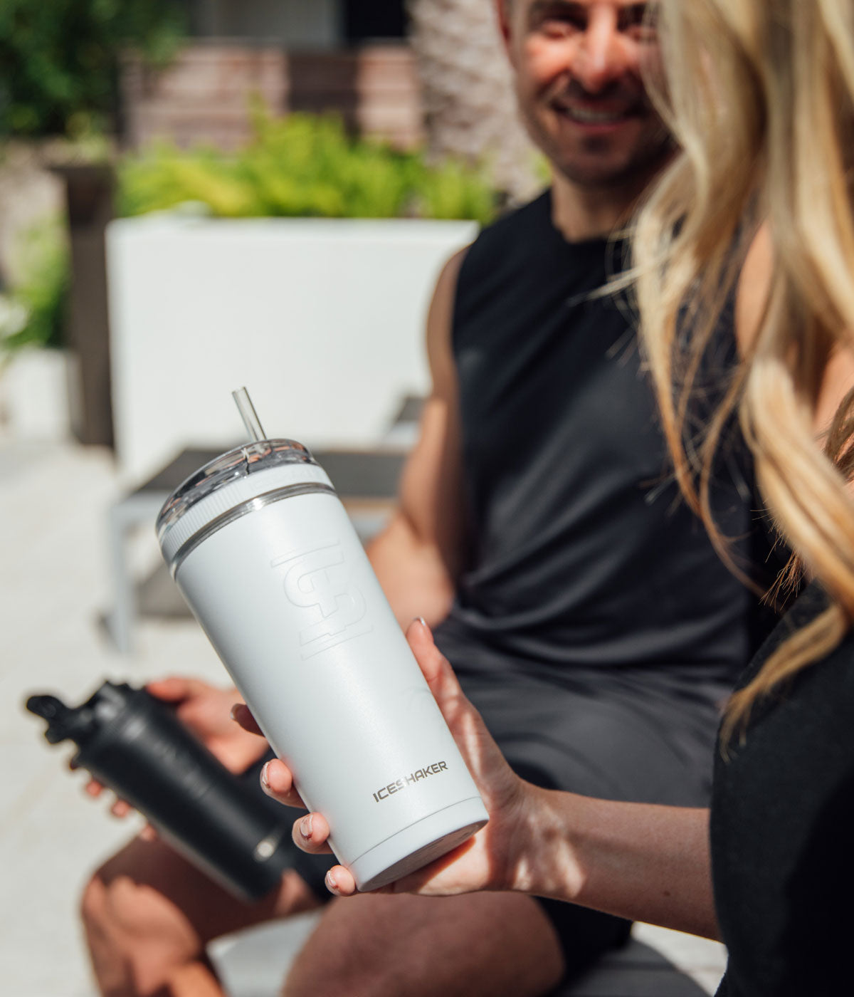 An image of a lady holding a white 26oz Flex Bottle with the straw in it. She is talking to a man in the background and he is smiling at her.