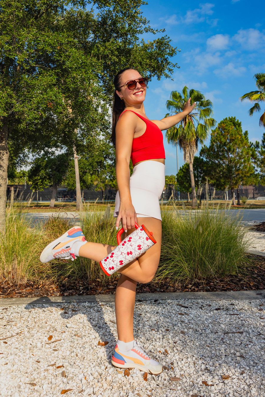Woman posing with a Ball Park Social tumbler by palm trees