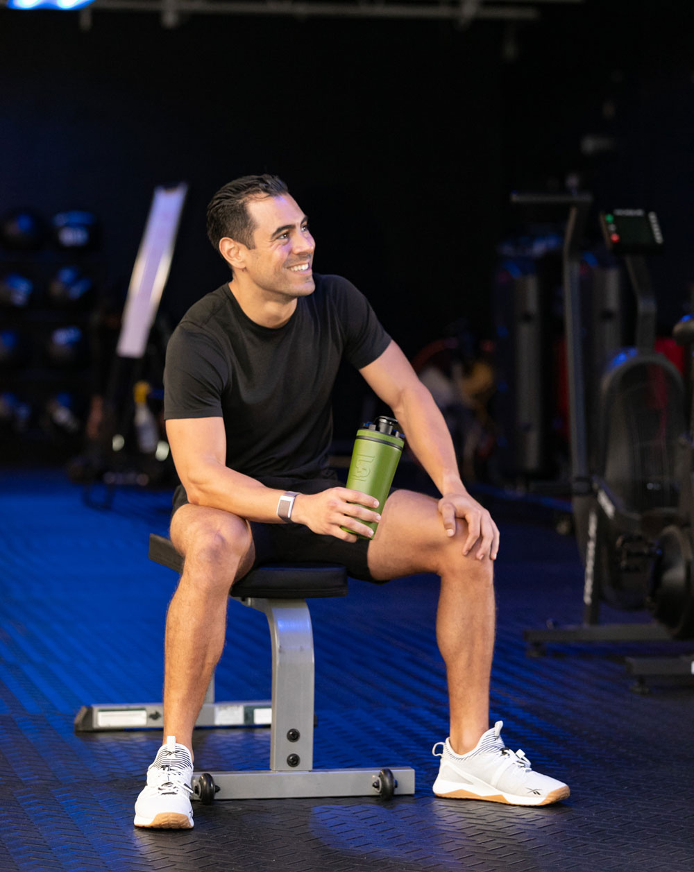 a man sitting down on a bench holding a green 26oz Shaker Bottle after a workout.