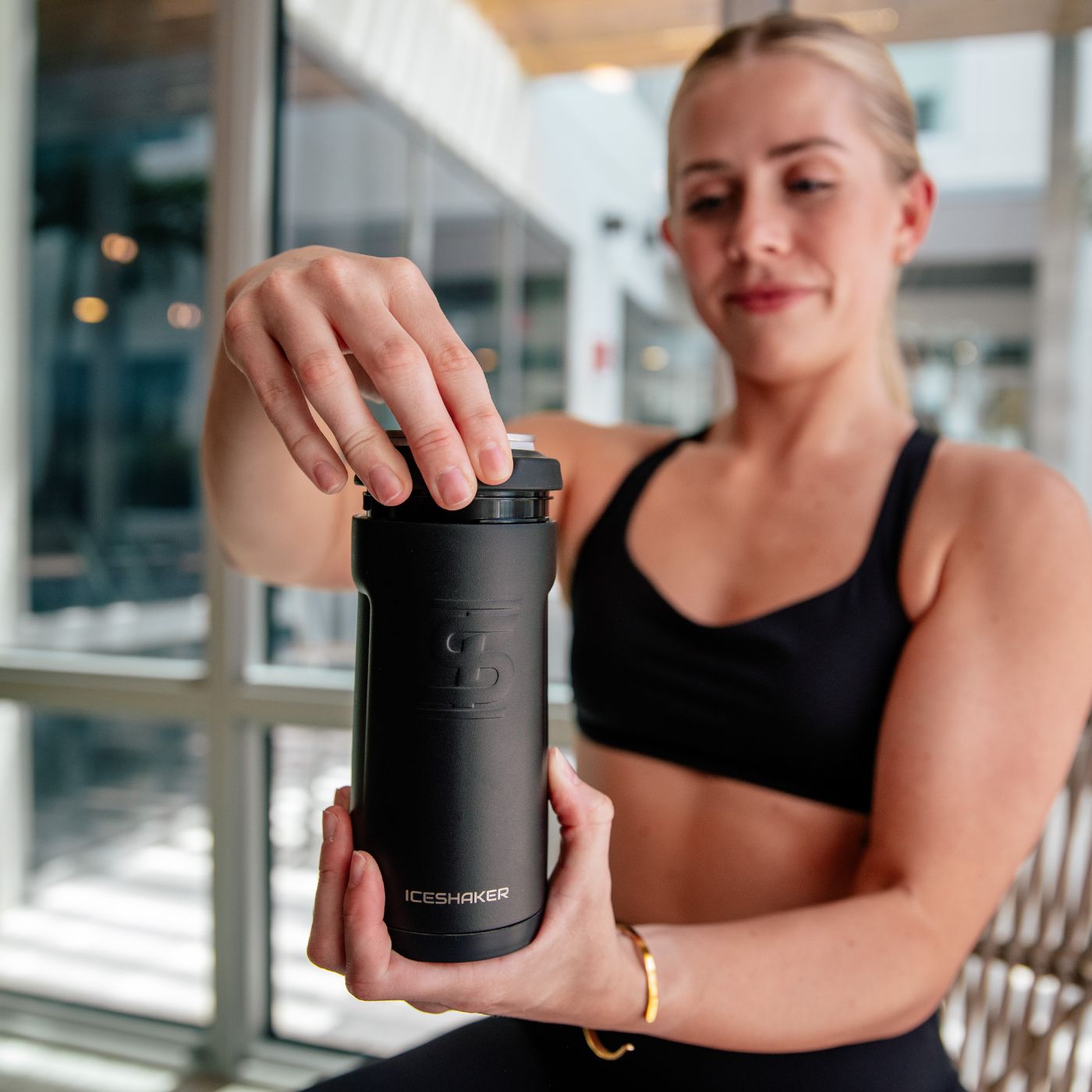 This image shows a young athletic woman twisting off the top rubber lid of the Ice Shaker Canpanion