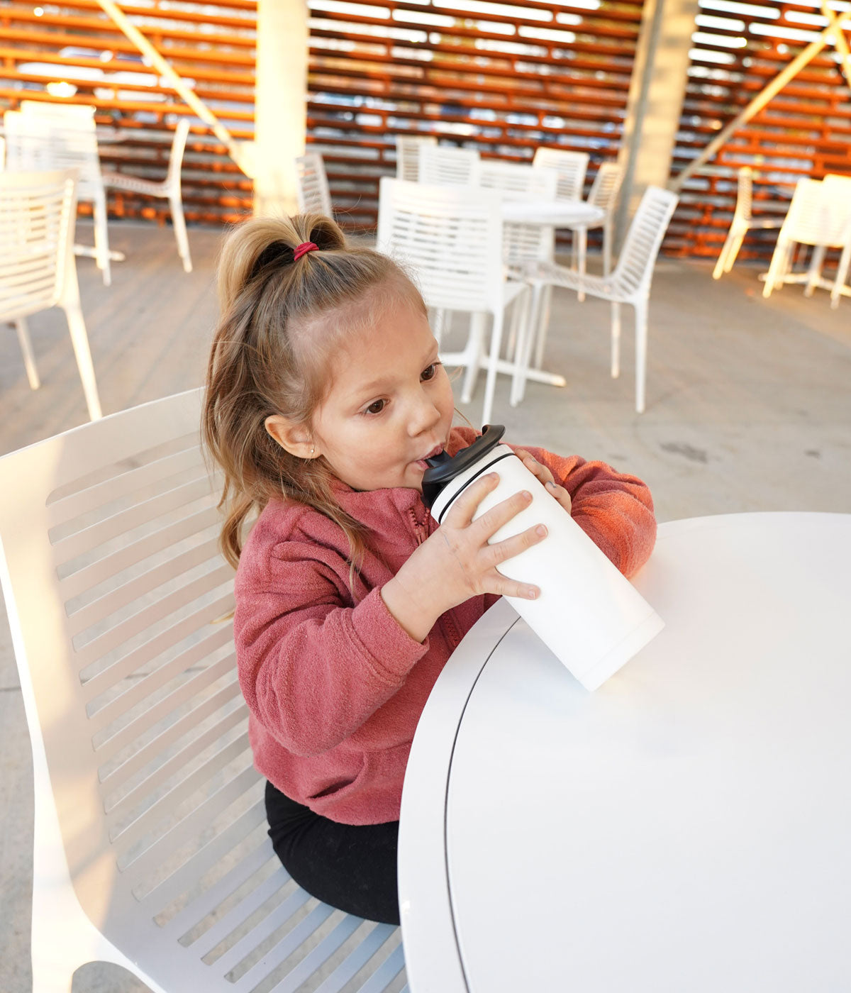 This image shows a little girl sitting at a table taking a drink from a White 14oz Sport Bottle