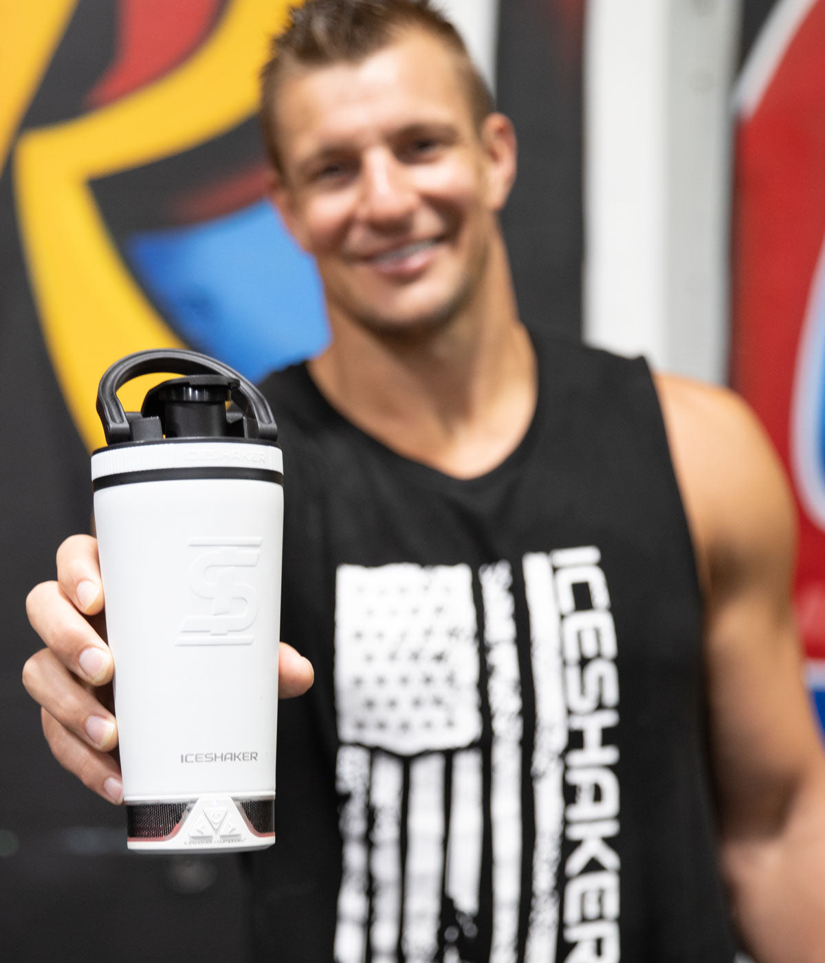 Former NFL Player, Rob Gronkowski has his arm stretch out towards the camera and he is holding a white 20oz Speaker Bottle