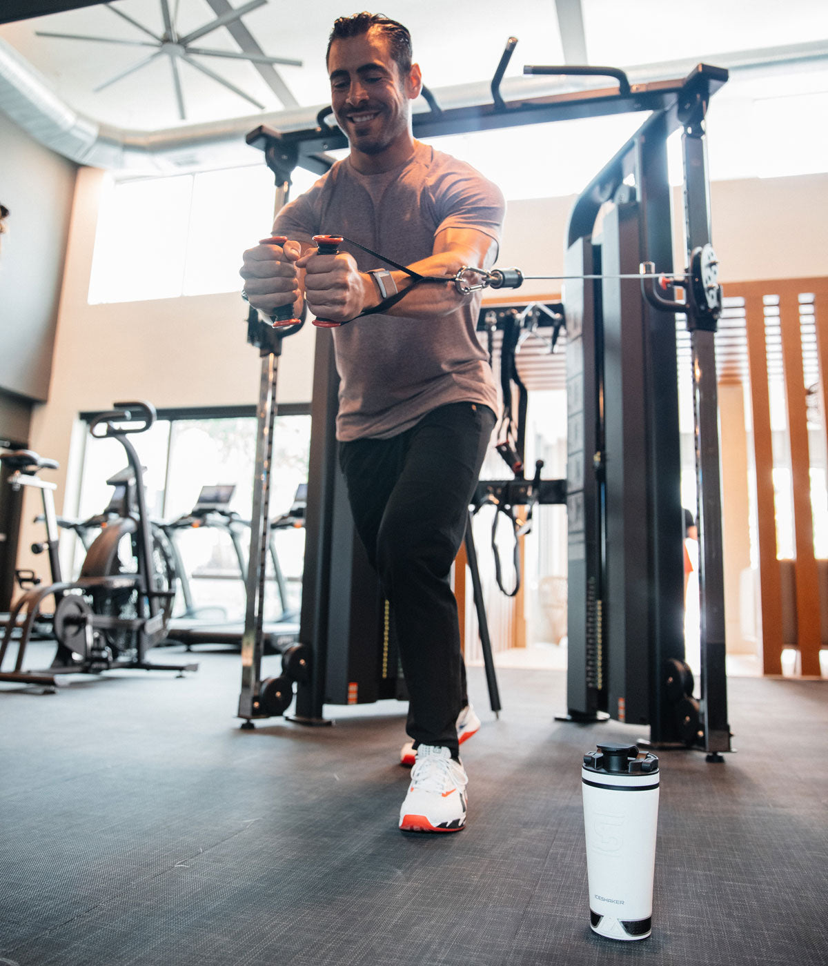 An image of a man working out on a workout machine. On the ground in front of him is a white 20oz Speaker Bottle