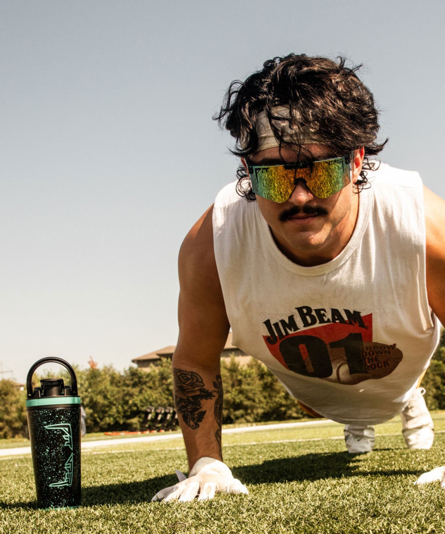 An image of a young Caucasian man doing a push up and looking at the camera. He is wearing a pair of Ice Shaker X Pit Viper sunglasses and has the Limited Edition Ice Shaker x Pit Viper 26oz Ice Shaker next to him. Click now to shop the Ice Shaker X Pit Viper Kit