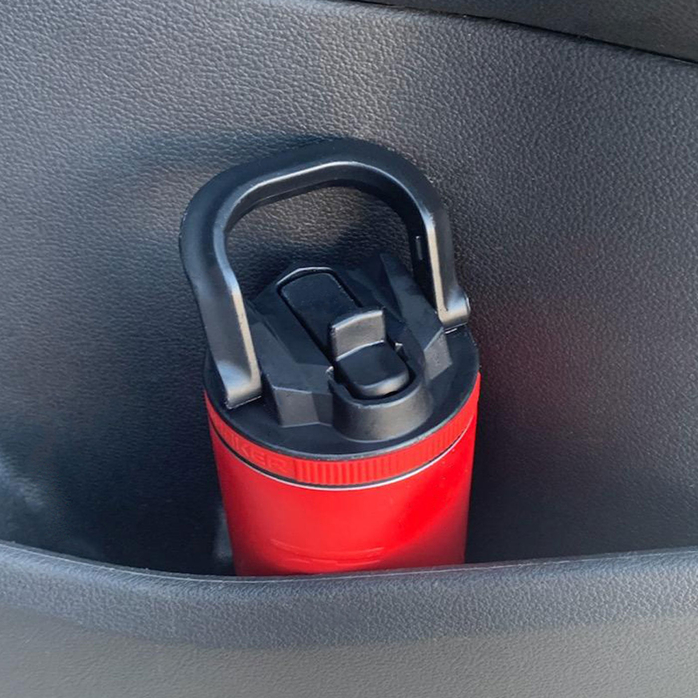This image shows a red 14oz Sport Bottle fitting easily in the cup holder in the back door of a car.