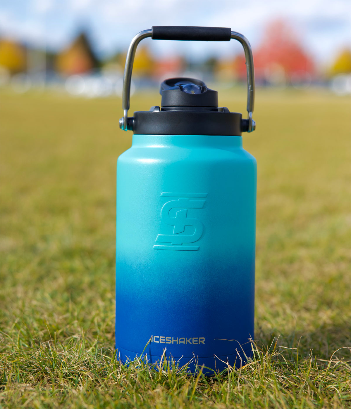 A navy mint ombre-colored One Gallon Jug sits in grass on a field.
