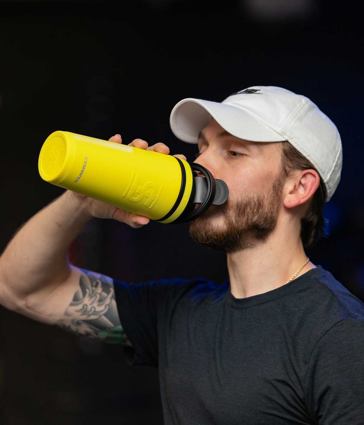 A young man is taking a drink from a Yellow 26oz Ice Shaker.