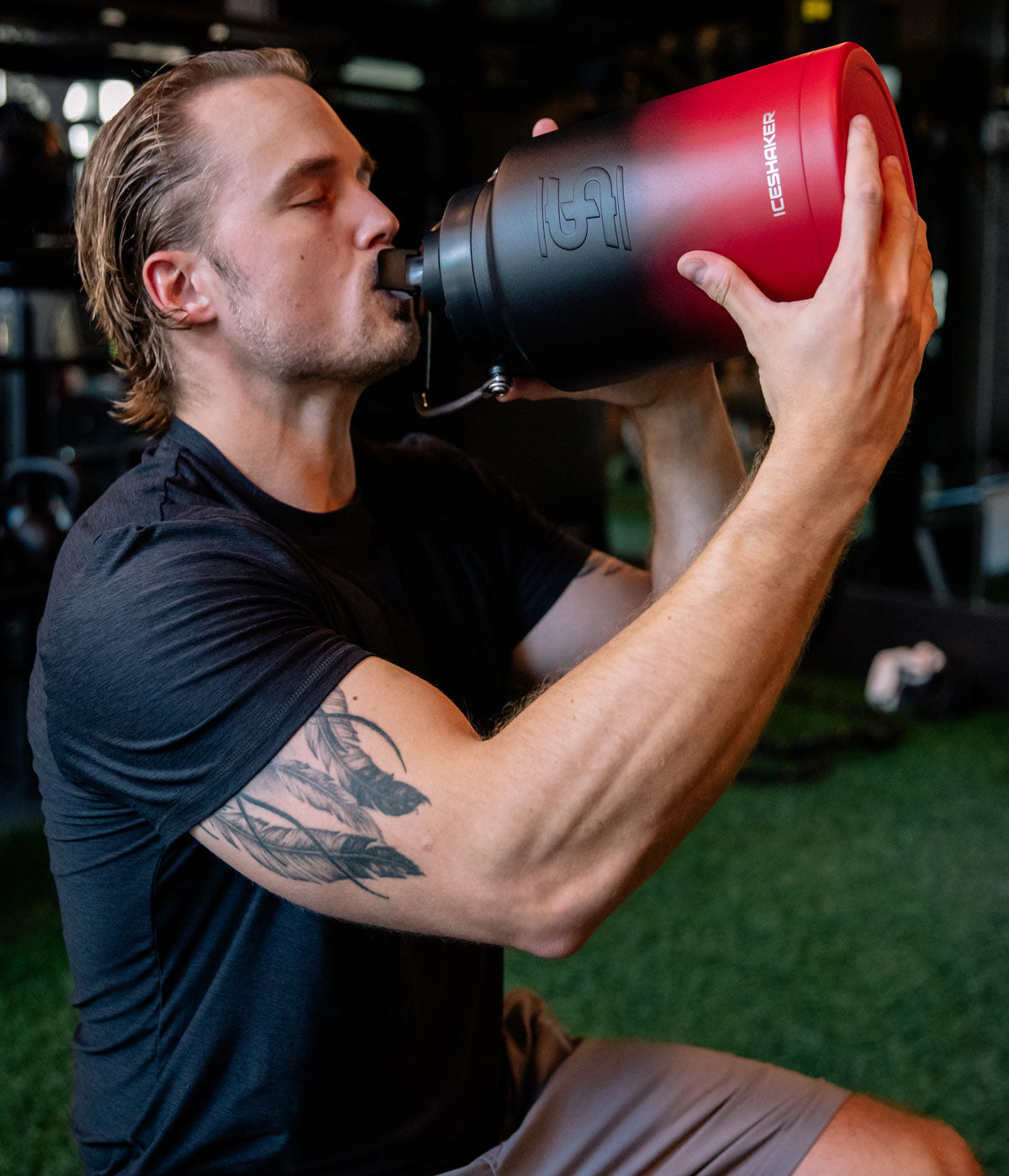 A man who has been working out takes a drink from a Red Black Ombre-colored One Gallon Jug.