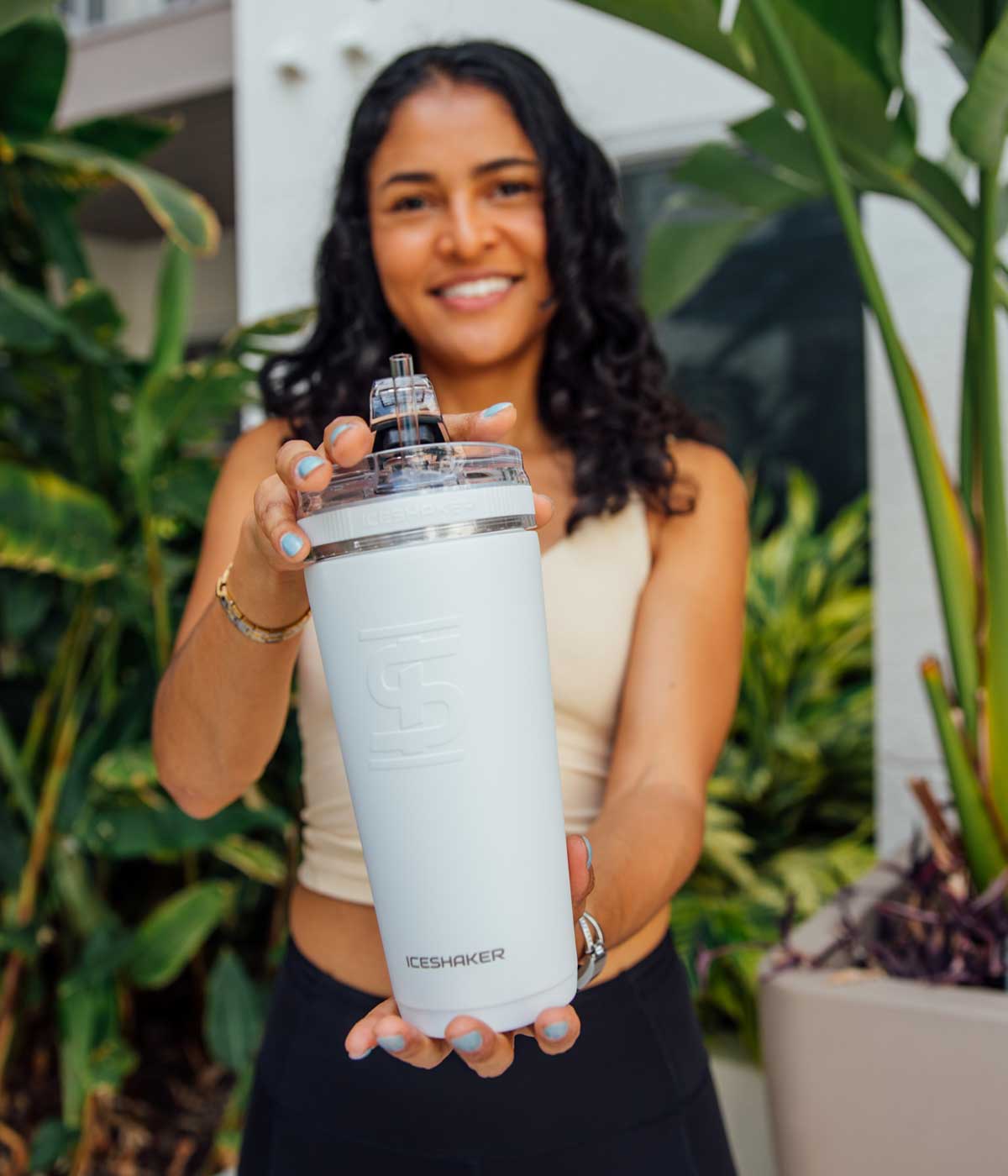 This image shows an athletic hispanic woman holding a white-colored 26oz Flex Bottle with both of her hands and her arms stretch out in front of her, showing the bottle to the camera