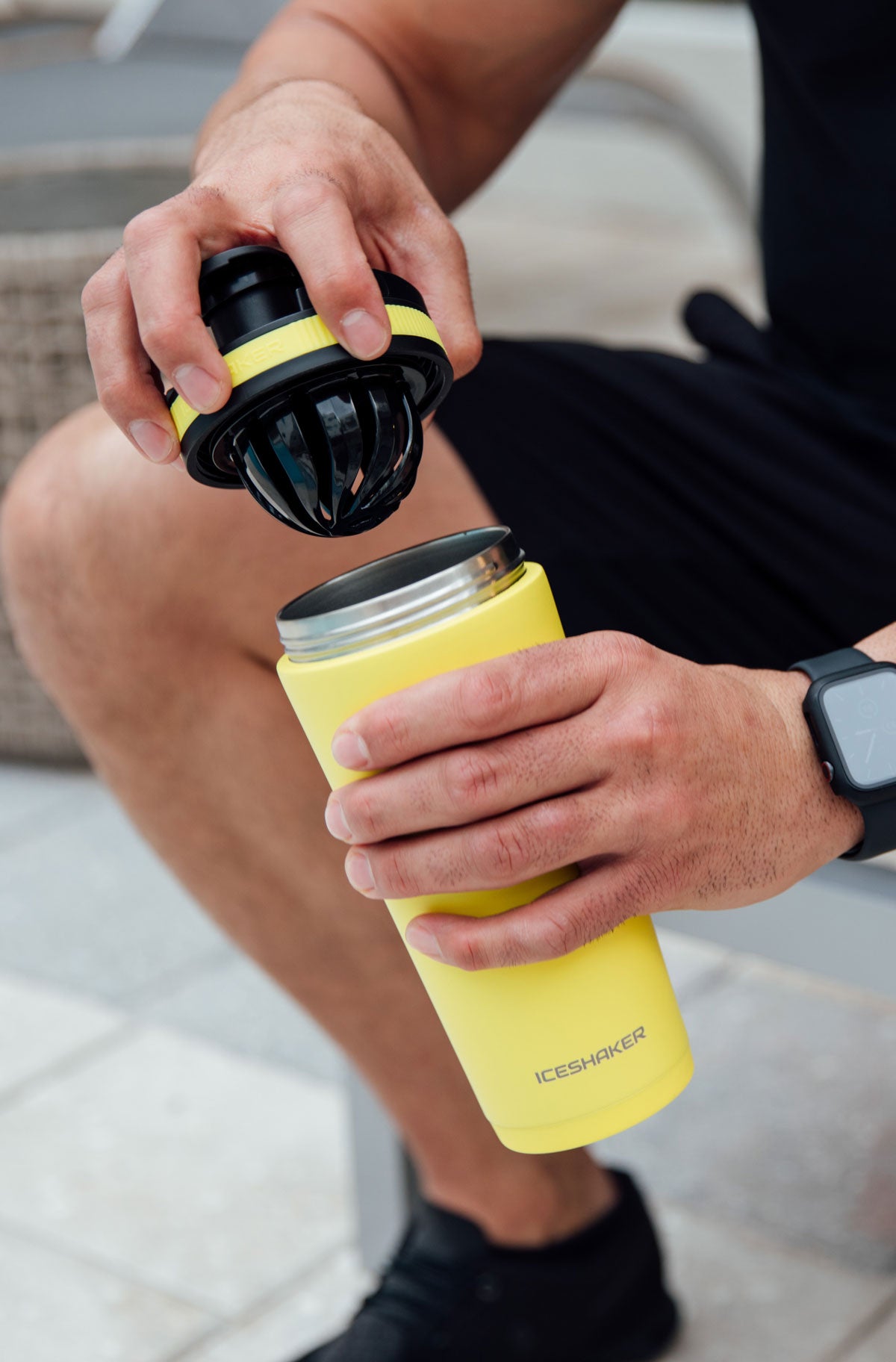 A close up image of the Yellow 26oz Ice Shaker as it is being opened by a male. In one hand he holds the patented agitator lid and in the other hand he holds the insulated bottle