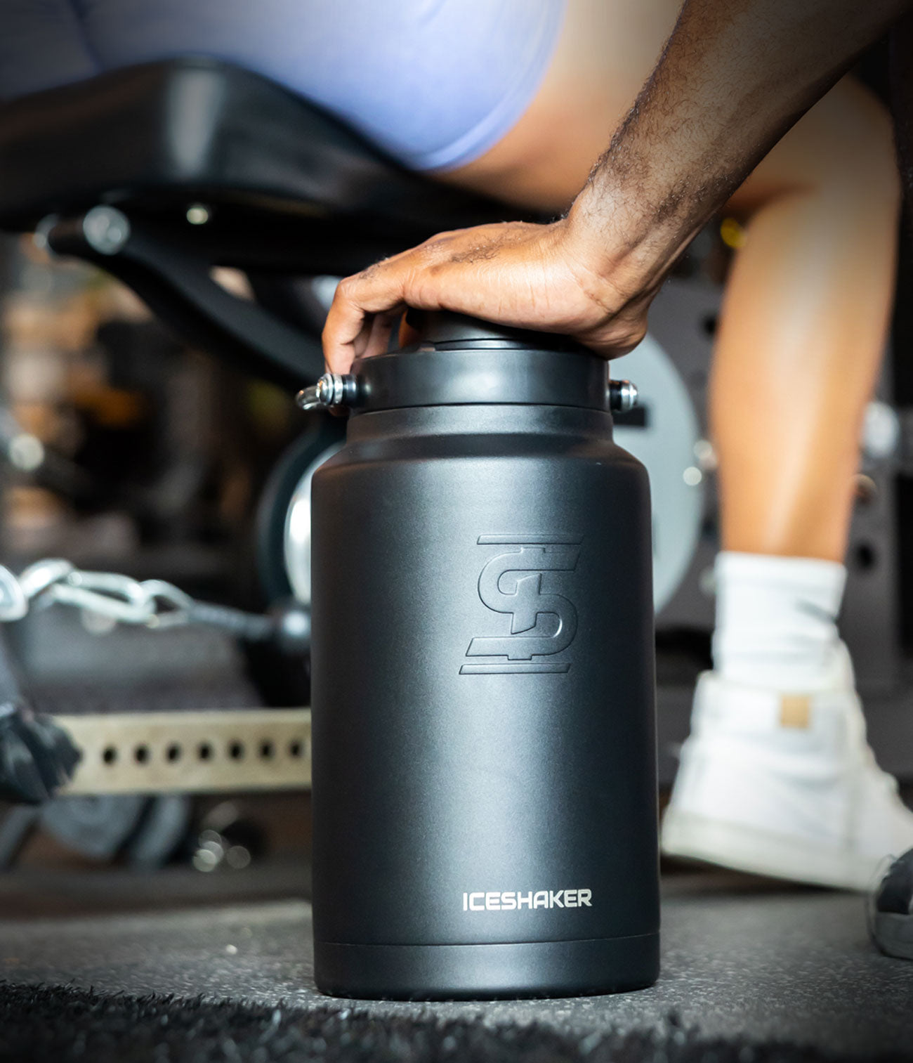 An image of a Black Ice Shaker One Gallon Jug sitting on a gym floor as people workout in the background.