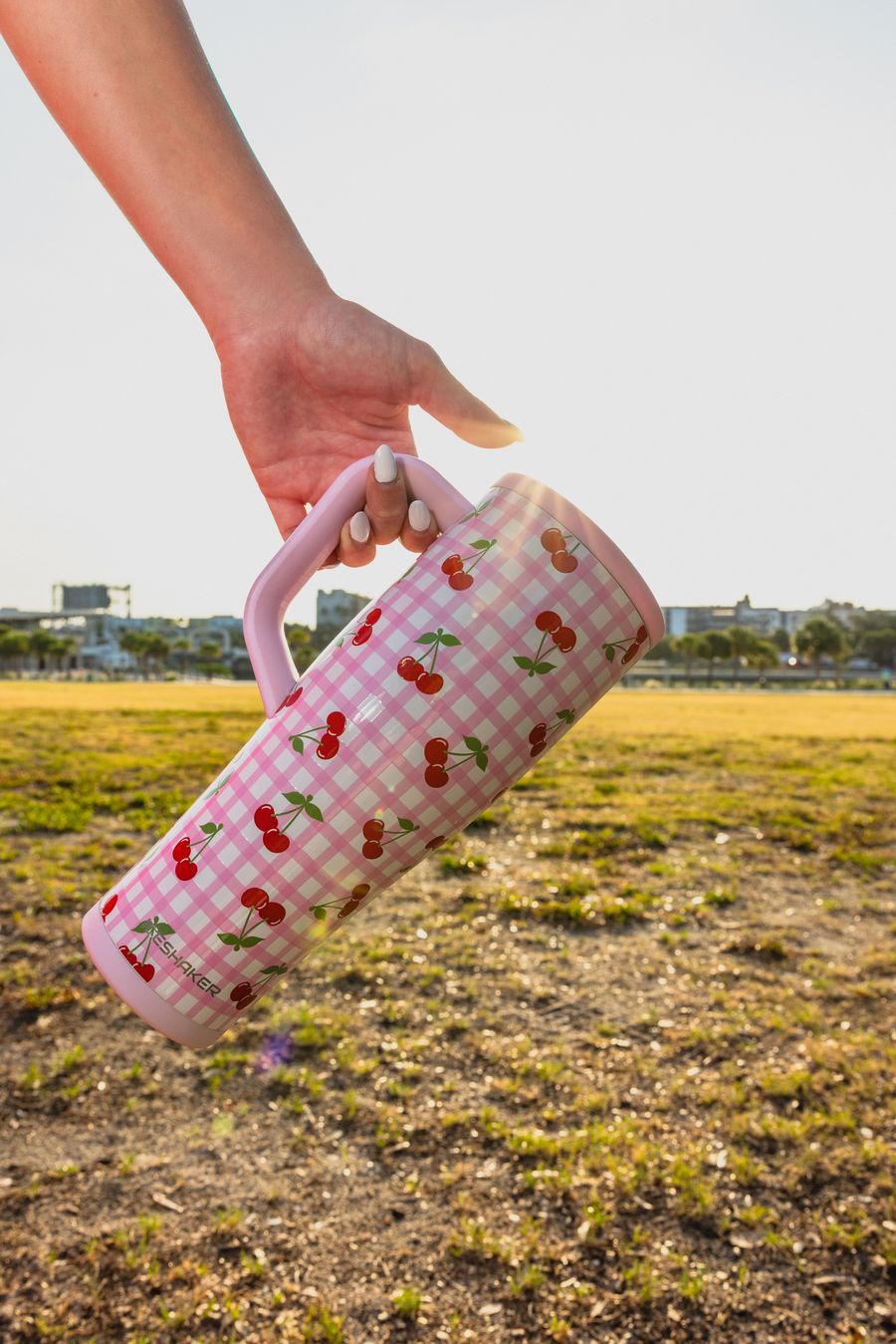 Hand carrying a Cherry Gingham tumbler by the handle over a field